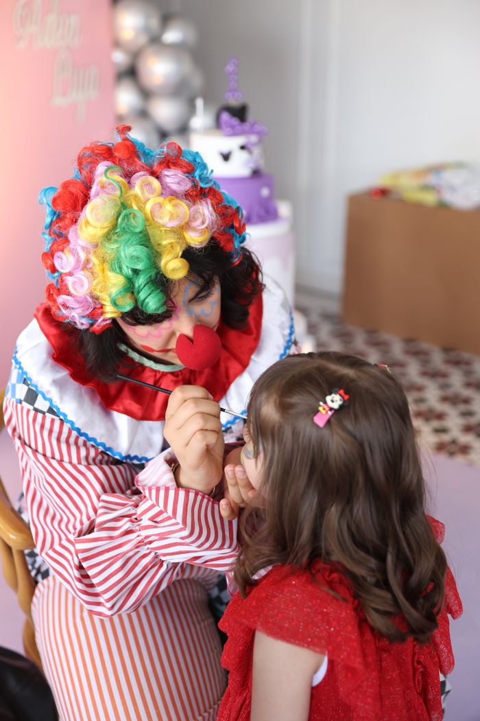 Clown face painting a girl at a lively children's party in Türkiye.