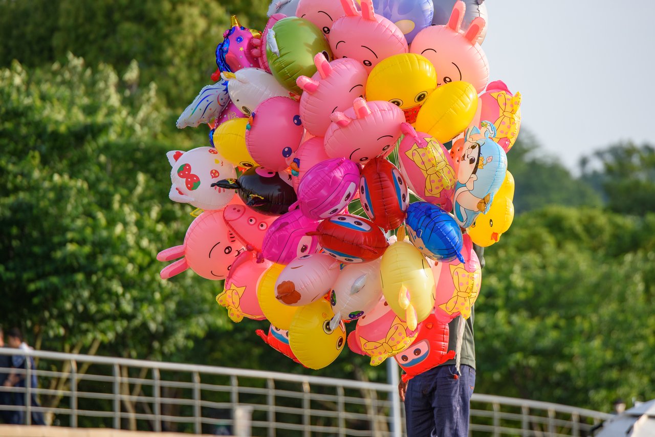 Vibrant cartoon character balloons being sold outdoors on a sunny day in a park.